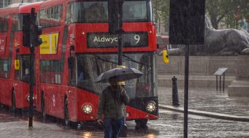 Londoner with umbrella and bus behind as heavy rain falls