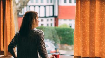 Woman stands at window of home